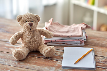 Image showing baby clothes, teddy bear toy and notebook