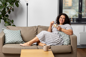 Image showing smiling young woman eating cake at home