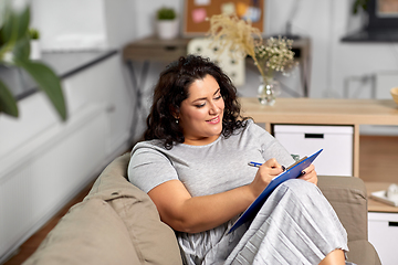 Image showing young woman with clipboard taking notes at home