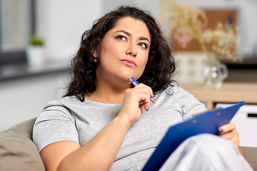 Image showing woman with clipboard and pen thinking at home