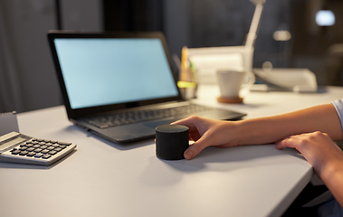 Image showing hand using smart speaker at night office