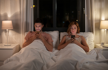 Image showing couple using smartphones in bed at night at home