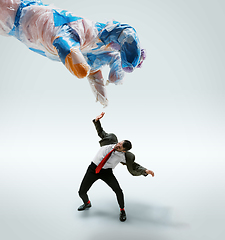 Image showing Young caucasian man avoiding big plastic hand on white studio background