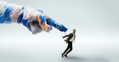 Image showing Young caucasian man avoiding big plastic hand on white studio background