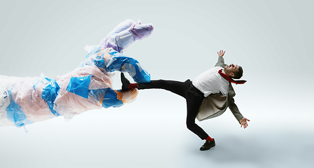 Image showing Young caucasian man avoiding big plastic hand on white studio background