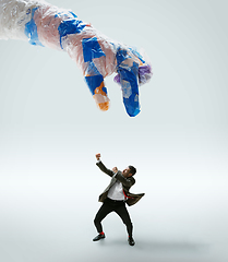 Image showing Young caucasian man avoiding big plastic hand on white studio background