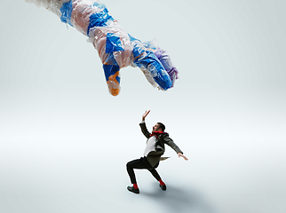 Image showing Young caucasian man avoiding big plastic hand on white studio background