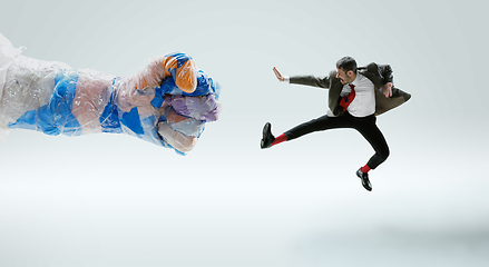 Image showing Young caucasian man avoiding big plastic hand on white studio background