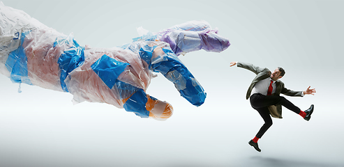 Image showing Young caucasian man avoiding big plastic hand on white studio background