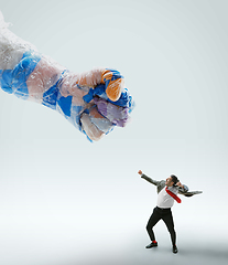 Image showing Young caucasian man avoiding big plastic hand on white studio background