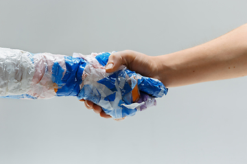 Image showing Big plastic hand made of garbage shaking another hand isolated on white studio background