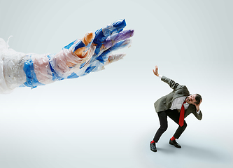 Image showing Young caucasian man avoiding big plastic hand on white studio background