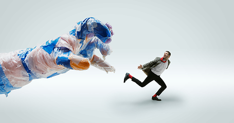 Image showing Young caucasian man avoiding big plastic hand on white studio background