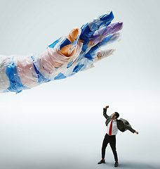 Image showing Young caucasian man avoiding big plastic hand on white studio background