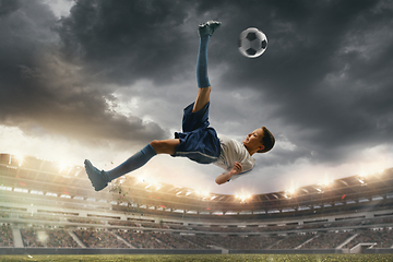 Image showing Young male soccer player kicking ball on stadium with flashlights on background