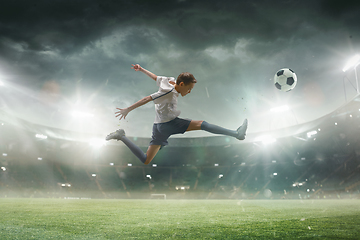 Image showing Young male soccer player kicking ball on stadium with flashlights on background