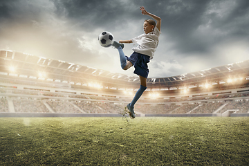 Image showing Young male soccer player kicking ball on stadium with flashlights on background