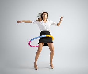 Image showing Caucasian woman in office clothes training with hoop isolated on grey studio background