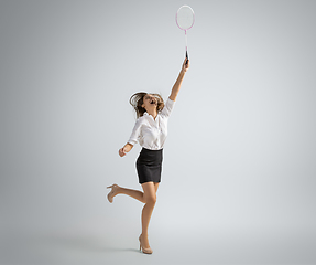Image showing Caucasian woman in office clothes plays badminton isolated on grey studio background