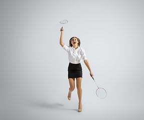 Image showing Caucasian woman in office clothes plays badminton isolated on grey studio background