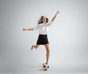 Image showing Caucasian woman in office clothes kicking ball isolated on grey studio background