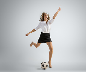 Image showing Caucasian woman in office clothes kicking ball isolated on grey studio background