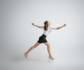 Image showing Caucasian woman in office clothes running isolated on grey studio background