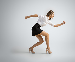 Image showing Caucasian woman in office clothes preparing to run isolated on grey studio background