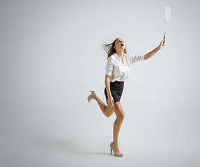 Image showing Caucasian woman in office clothes plays badminton isolated on grey studio background