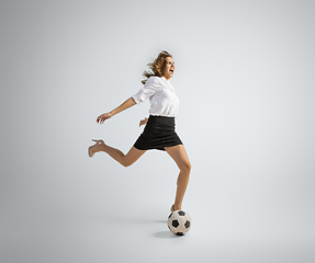 Image showing Caucasian woman in office clothes kicking ball isolated on grey studio background