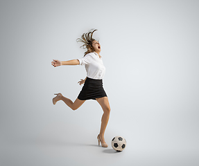 Image showing Caucasian woman in office clothes kicking ball isolated on grey studio background