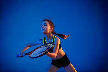 Image showing Little caucasian girl playing tennis isolated on blue background in neon light