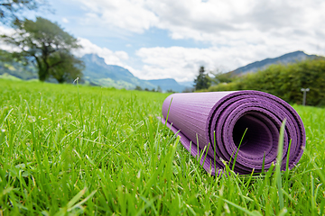 Image showing Rolled up fitness mat on the green grass background