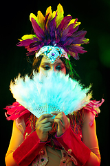 Image showing Beautiful young woman in carnival mask and masquerade costume in colorful lights