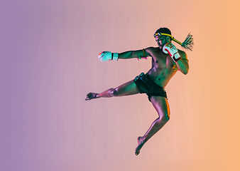 Image showing Muay thai. Young man exercising thai boxing on gradient background