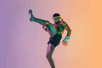 Image showing Muay thai. Young man exercising thai boxing on gradient background