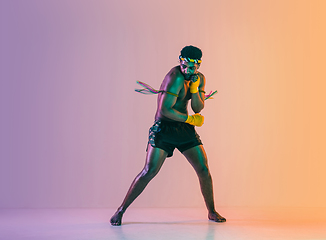 Image showing Muay thai. Young man exercising thai boxing on gradient background