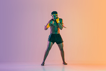 Image showing Muay thai. Young man exercising thai boxing on gradient background