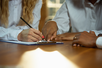 Image showing Close up of african-american and caucasian human\'s hands writing on sheets on wooden table