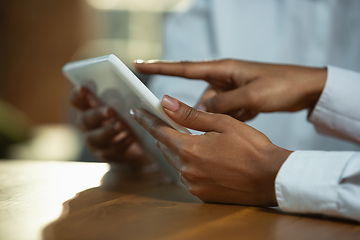 Image showing Close up of african-american human\'s hands using tablet on wooden table