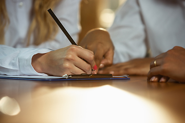 Image showing Close up of african-american and caucasian human\'s hands writing on sheets on wooden table