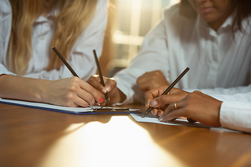 Image showing Close up of african-american and caucasian human\'s hands writing on sheets on wooden table