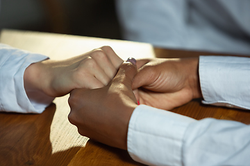 Image showing Close up of african-american and caucasian human\'s hands holding on wooden table