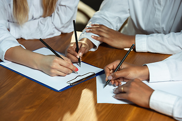 Image showing Close up of african-american and caucasian human\'s hands writing on sheets on wooden table