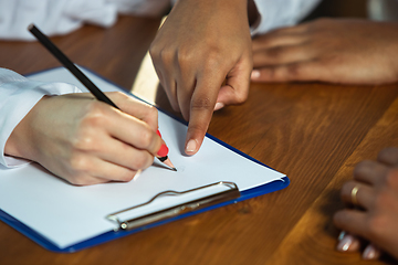 Image showing Close up of african-american and caucasian human\'s hands writing on sheets on wooden table