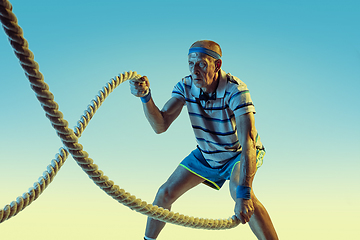 Image showing Senior man training with ropes in sportwear on gradient background and neon light