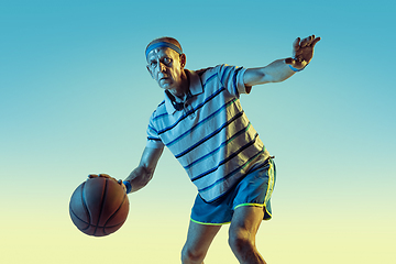 Image showing Senior man playing basketball in sportwear on gradient background and neon light