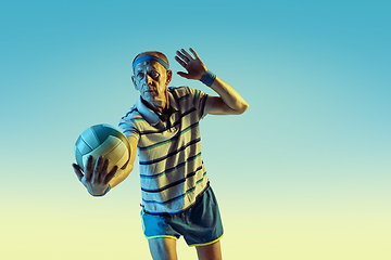 Image showing Senior man playing volleyball in sportwear on gradient background and neon light