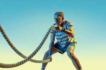 Image showing Senior man training with ropes in sportwear on gradient background and neon light