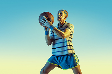 Image showing Senior man playing basketball in sportwear on gradient background and neon light